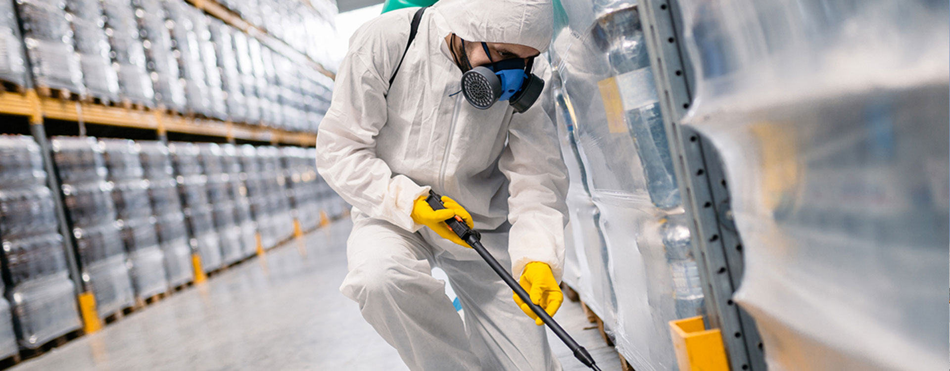 Dedetizadora em Brasília. Dedetização no DF. Dedetizador, trajando roupa de proteção branca com máscara de proteção facial, aplicando produtos em um galpão de estoque de produtos